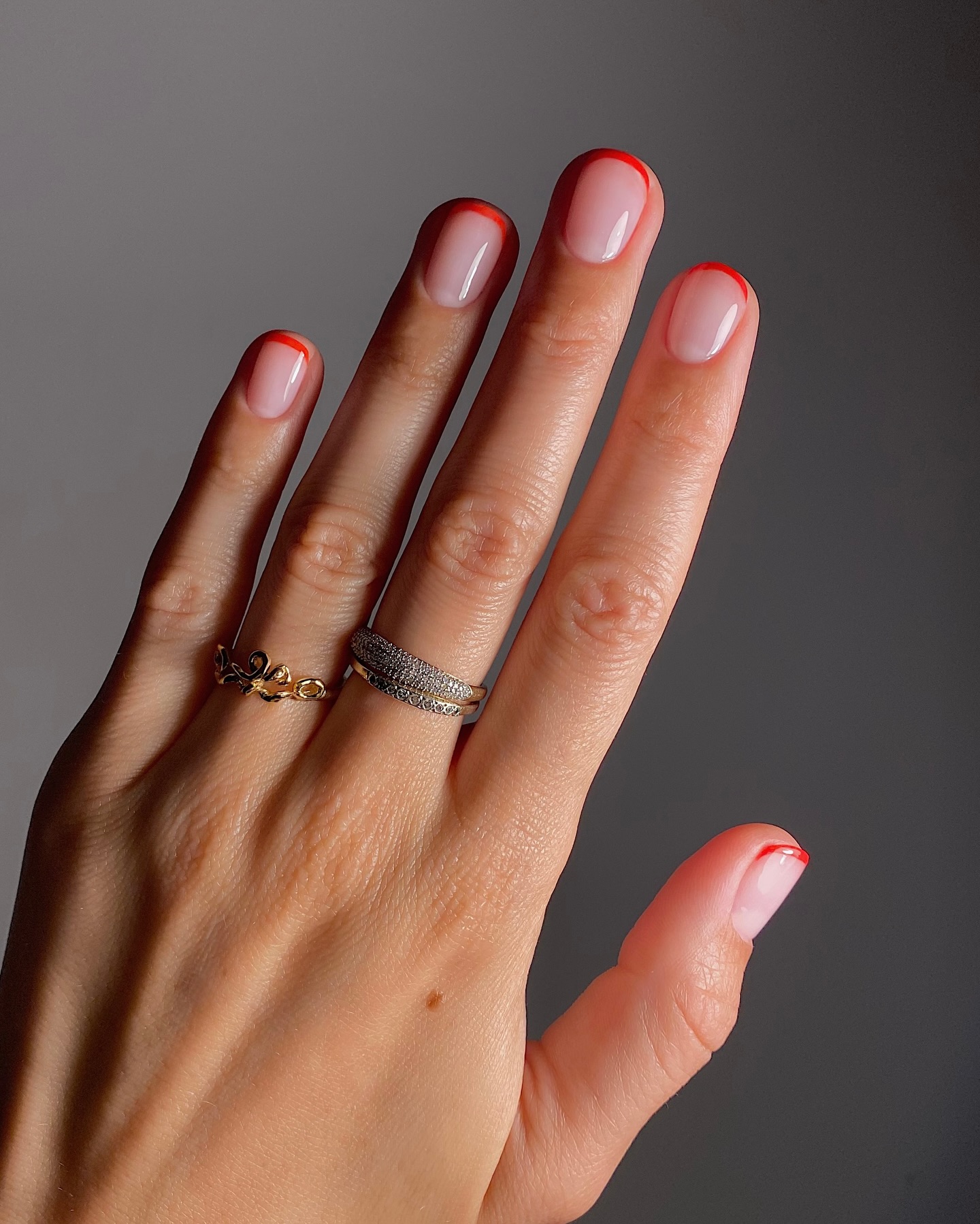 Photo of a red French manicure in front of a gray wall