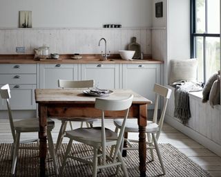 A grey rustic kitchen with wall paneling, dining table and chairs and window seat in corner
