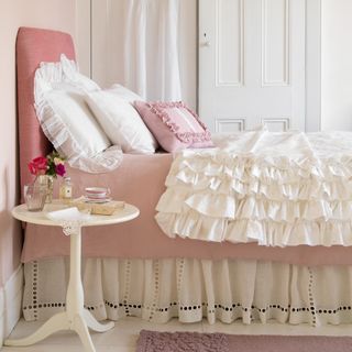 Side of a bed with ruffled and pink bedding and headboard