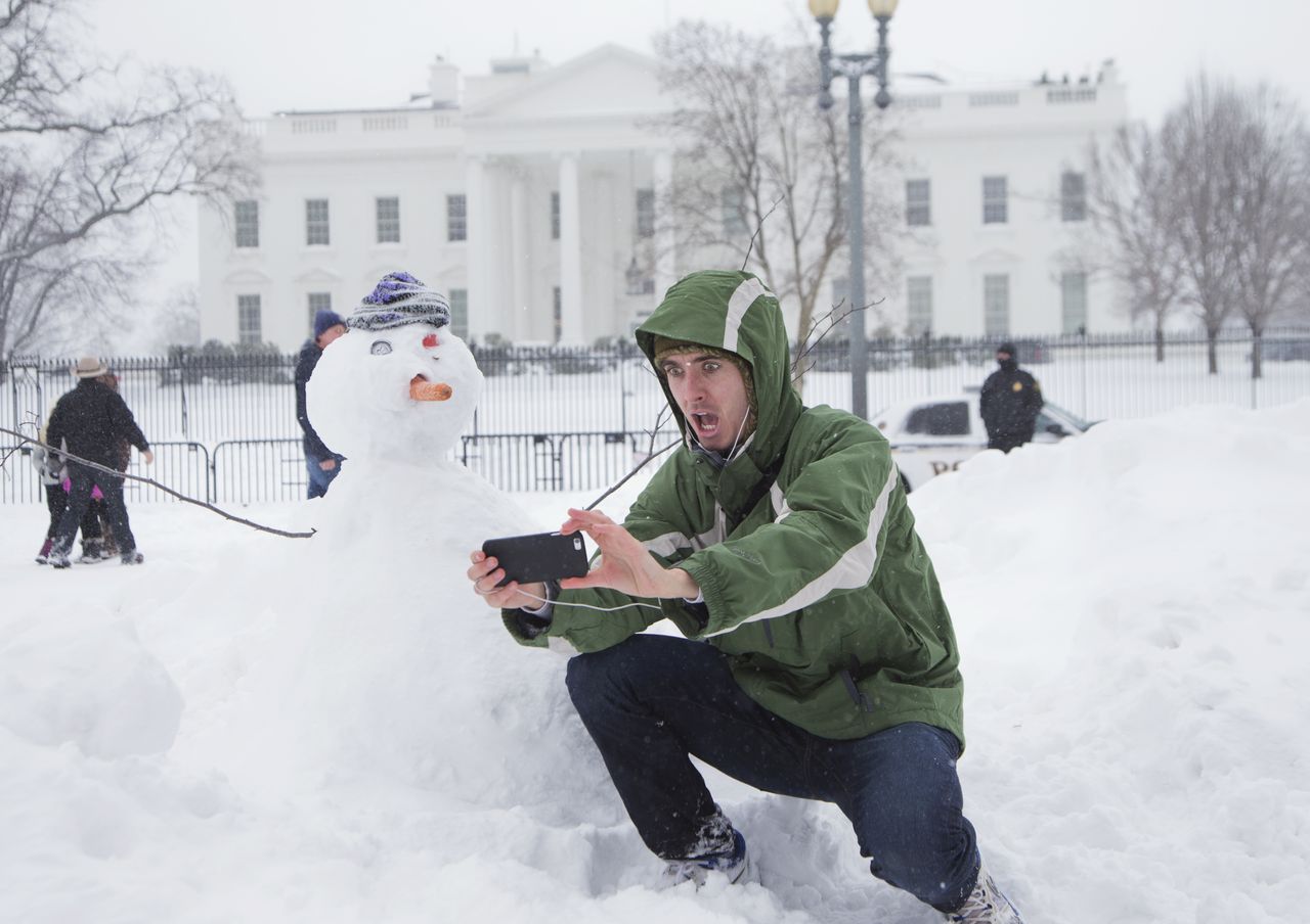 A man takes a selfie with a snowman in front of the White House