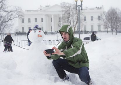A man takes a selfie with a snowman in front of the White House