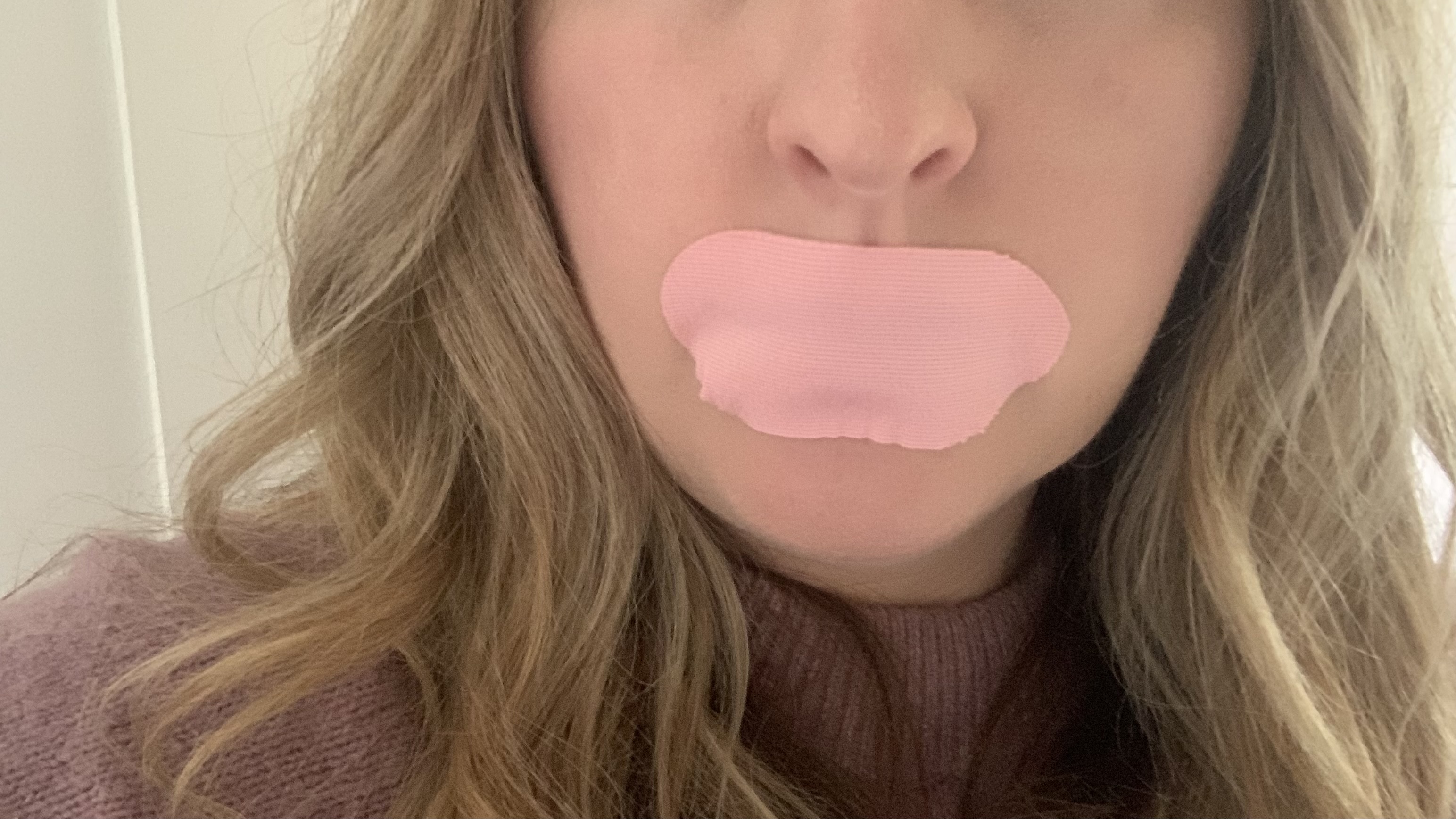 A close up of Pink mouth tape stuck over a woman's mouth