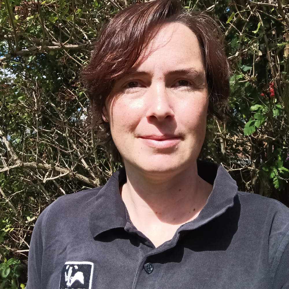 female with short hearing wearing navy polo shirt stood in front of trees