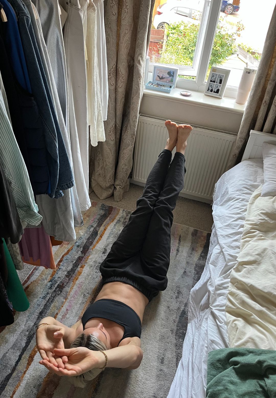 A woman practices a hollow hold Pilates exercise on her bedroom floor