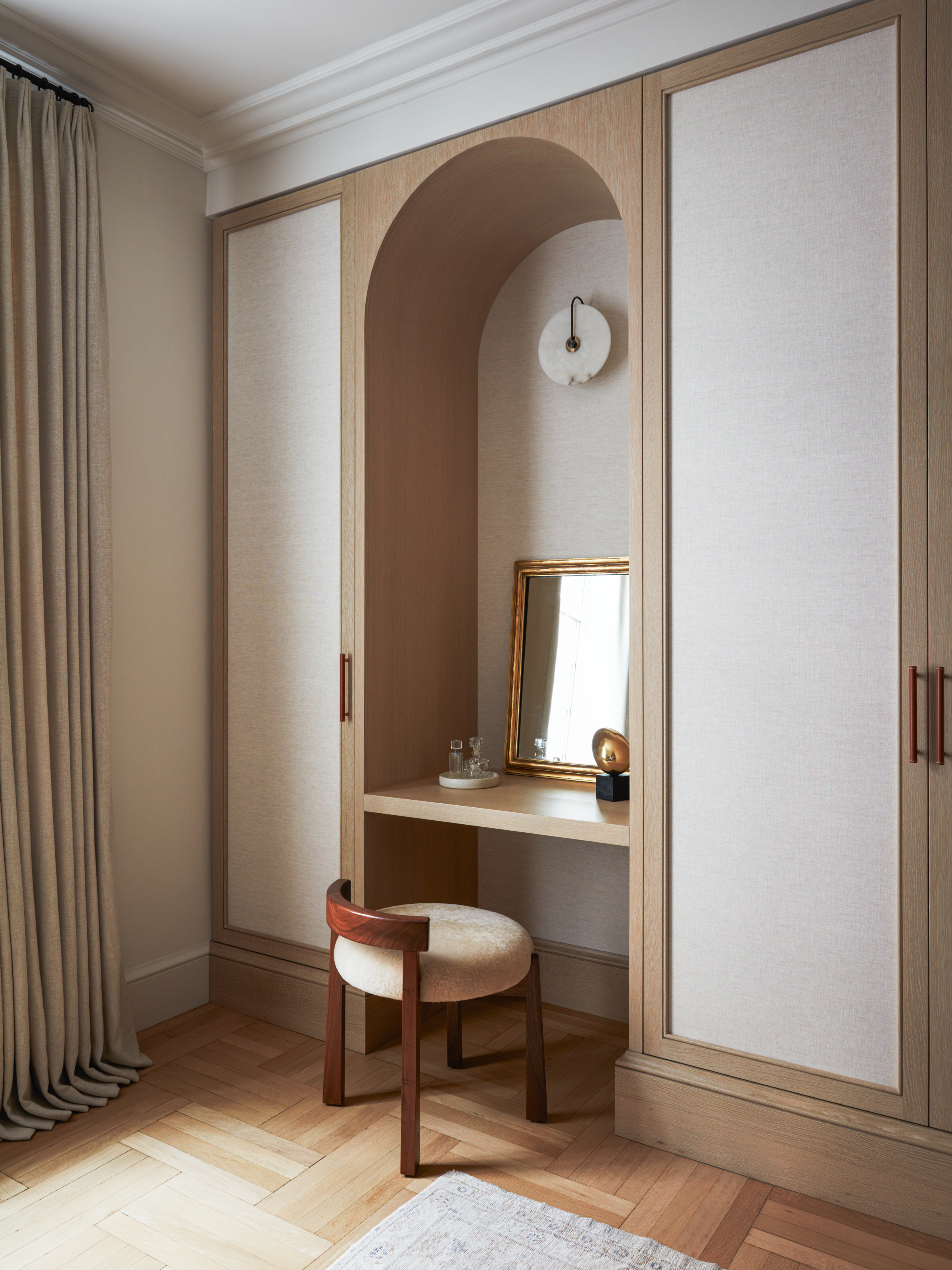 Dressing area with pale oak and canvas joinery, arched desk area with dark wood and cream upholstered stool, and parquet flooring