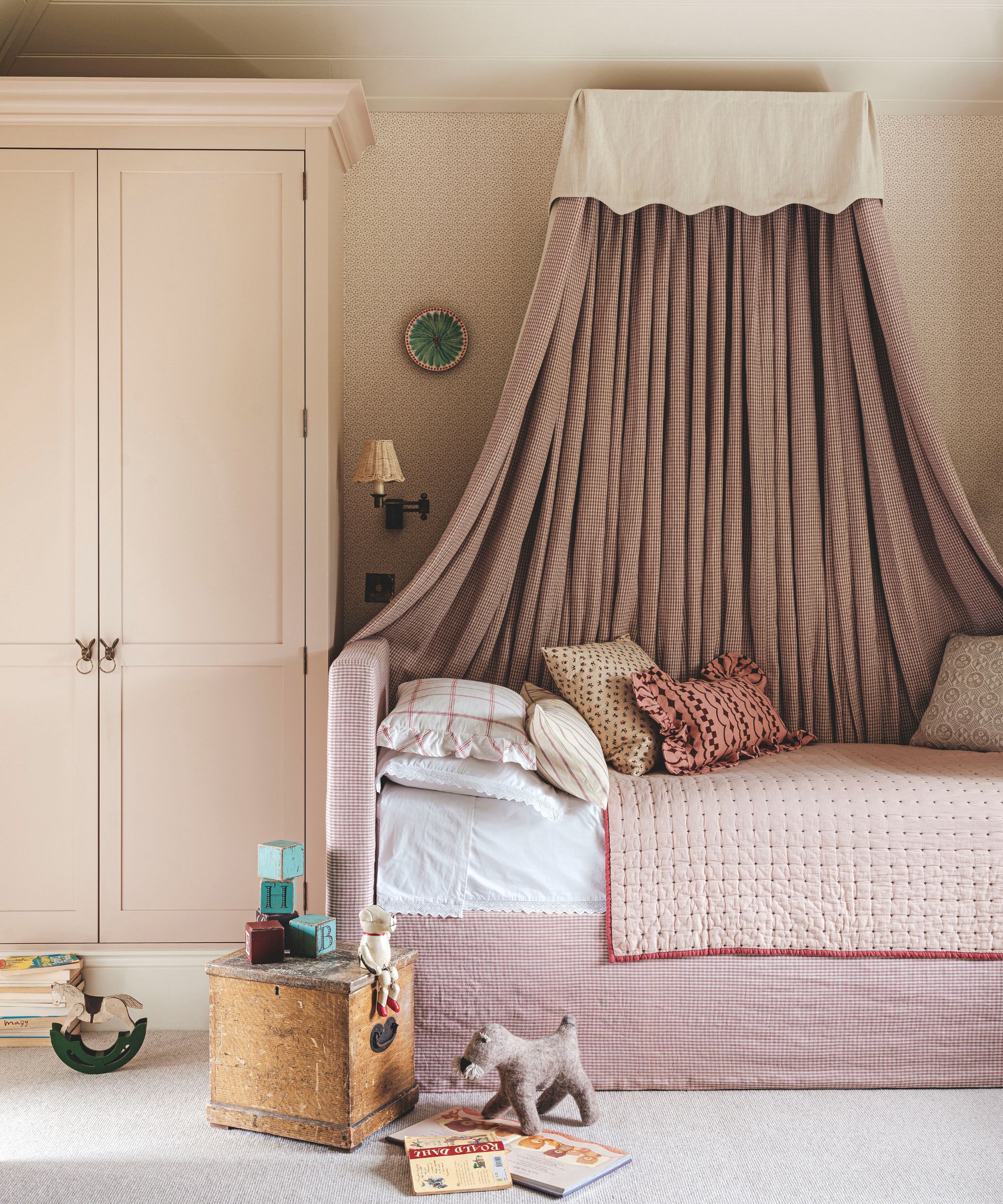 A charming child&amp;rsquo;s bed nook featuring a draped pink-and-white checkered canopy, a matching pleated bed skirt, and a light pink wardrobe.