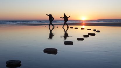 Two people traverse water by stepping on rocks set up like stepping stones.