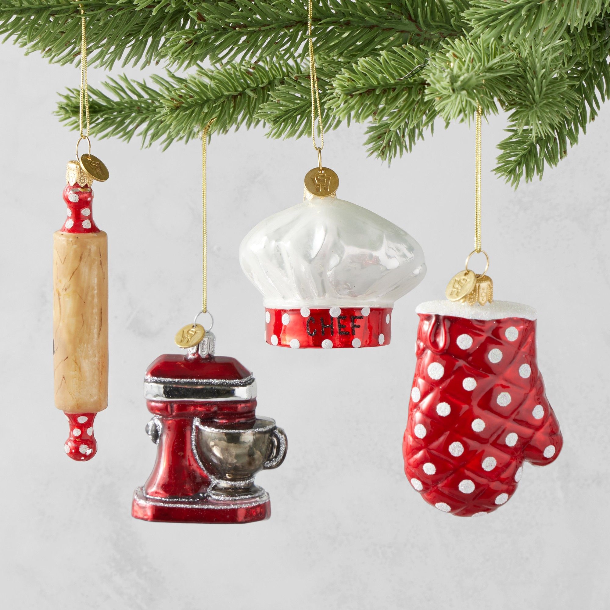Red and white glass Christmas ornaments in the shape of an oven mitt, chef's hat, stand mixer and rolling pin
