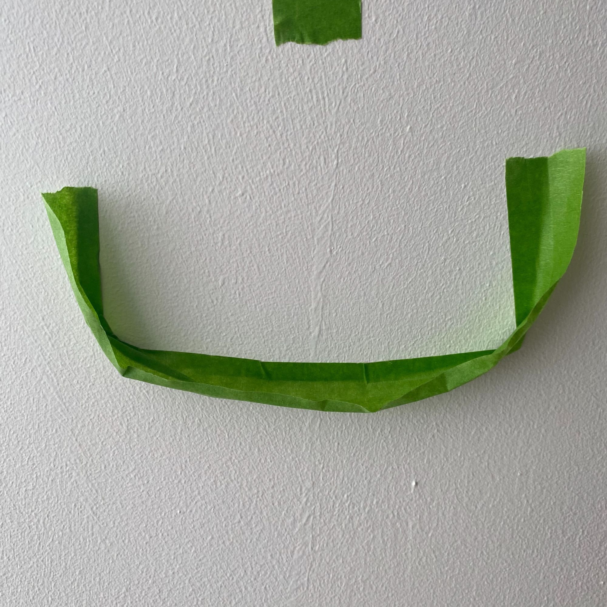 Masking tape dust catcher attached to a white wall beneath where the hole is to be drilled