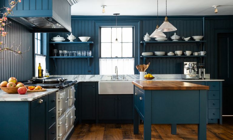 dark blue kitchen with tongue and groove walls and cabinets, blue island, glass pendants and white range cooker 