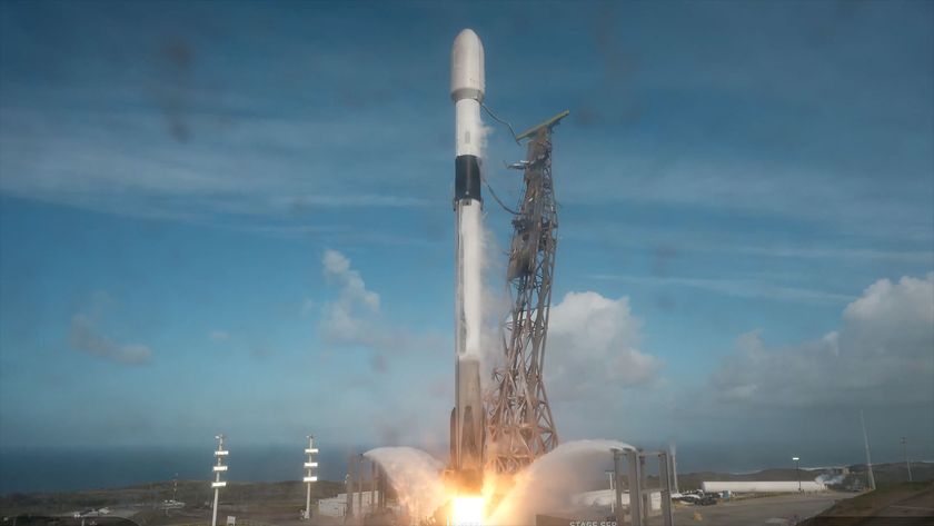A white and black rocket lifts off from its launch pad into a partially cloudy blue sky.