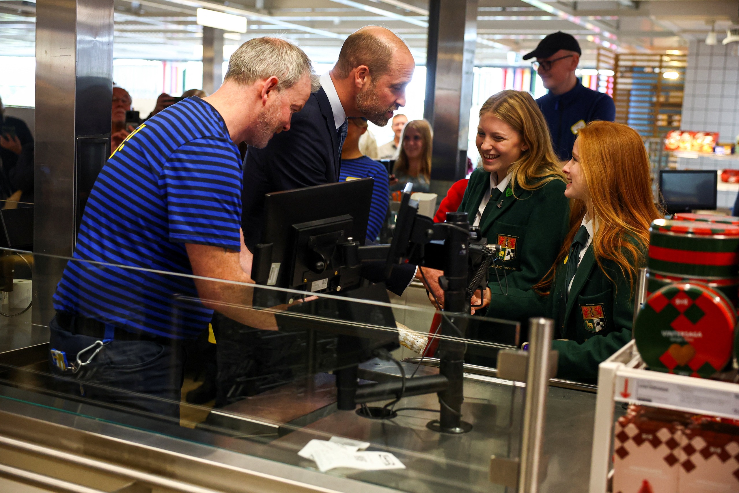 Prince William talking to two school girls as he works at an IKEA cash register