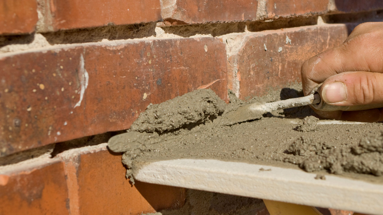 Close up of grey mortar being applied to red brick repointing brickwork