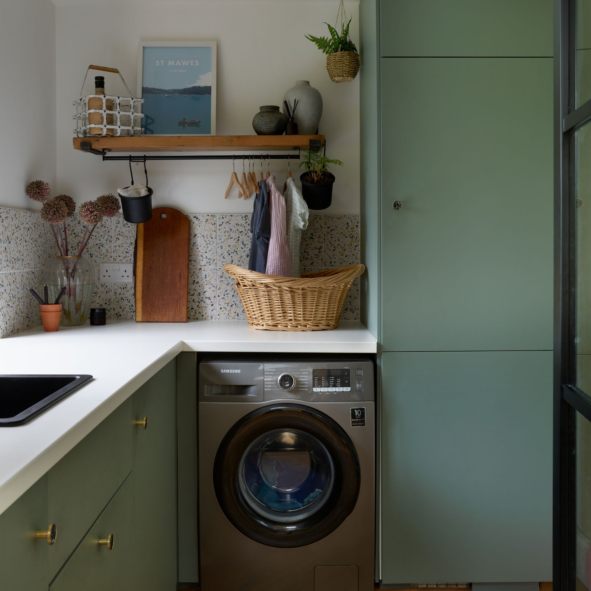 Utility room with green cabinets and terrazzo tiled backsplash, and white worktop