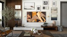 A living room with an art tv and a gallery wall with art work framed around it. There is also a large plant beside the gallery wall in a large white pot as well as a view of a coffee table with books and other essentials 