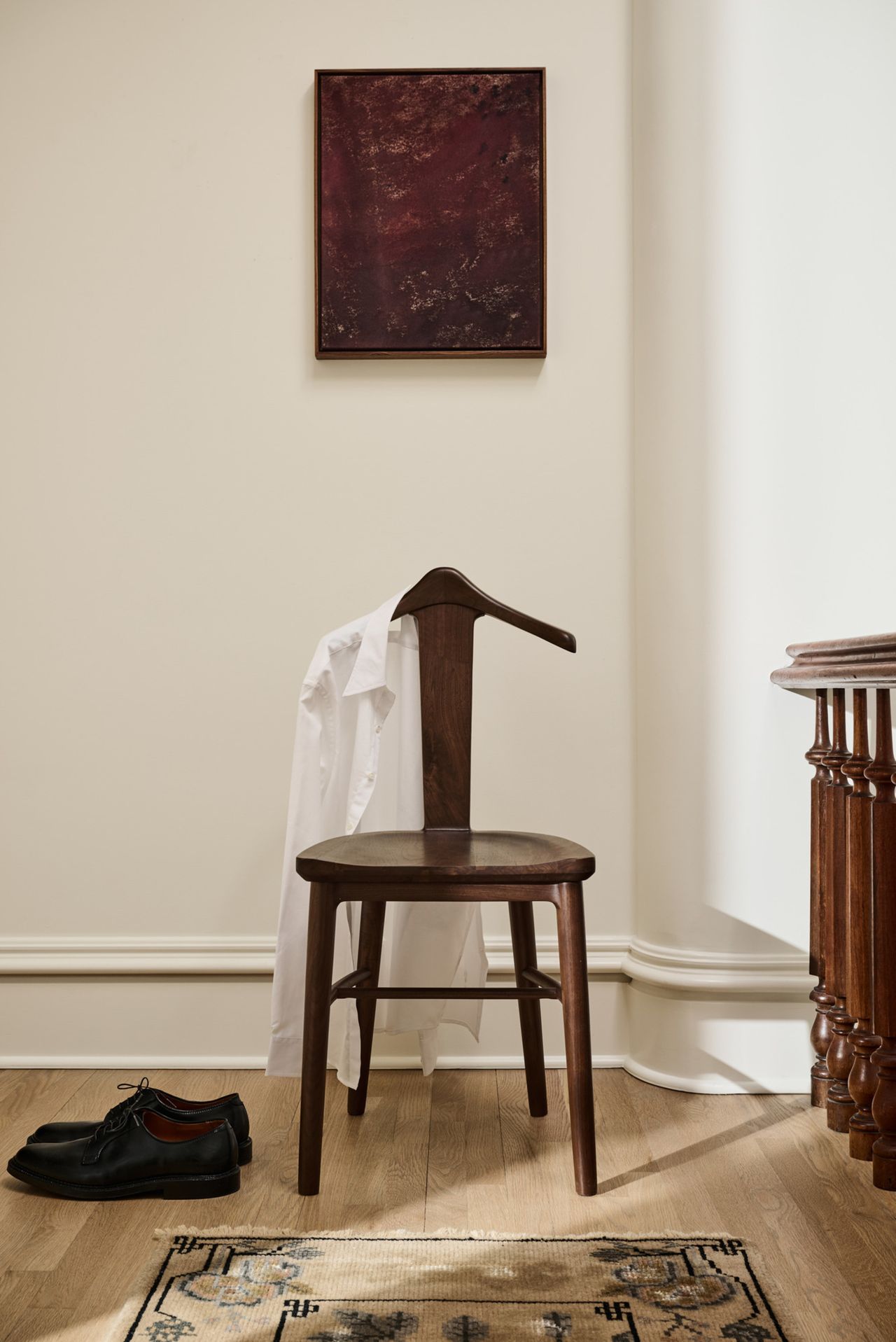 A wooden chair that's back is shaped like a hanger in a white room.