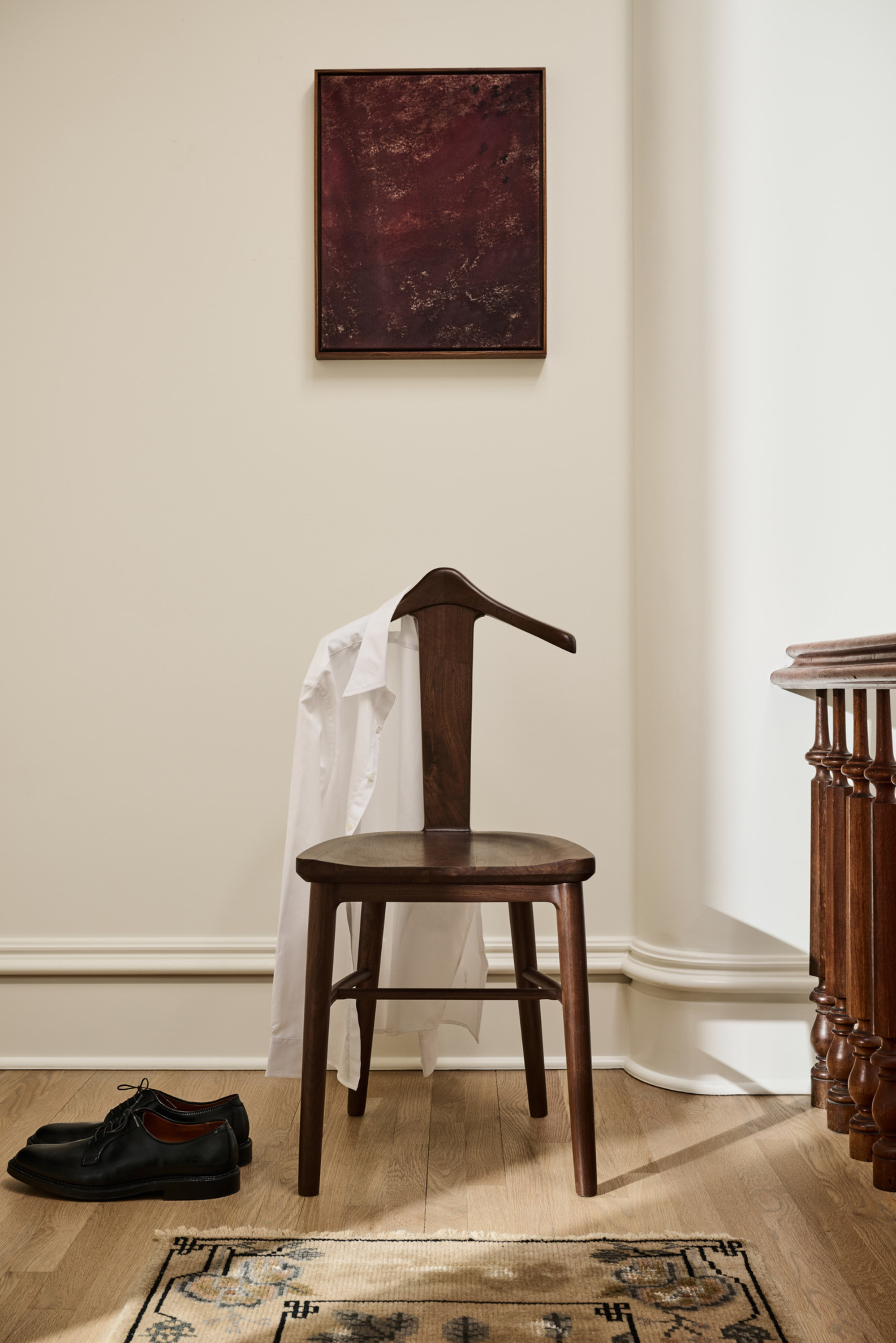 A wooden chair that's back is shaped like a hanger in a white room. 