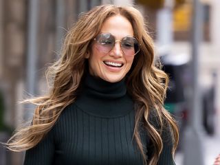Jennifer Lopez looks away from the camera and smiles wearing large sunglasses.