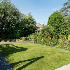 Cut grass lawn in garden surrounded by border plants and trees