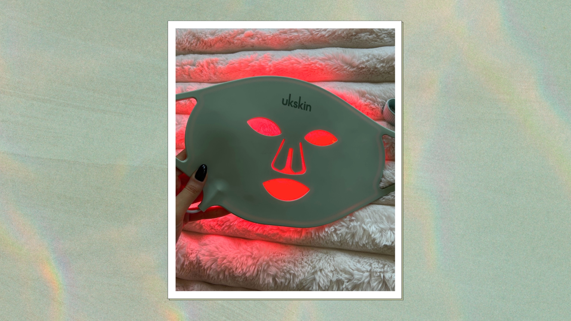 Hand holding the UKLASH LED mask whilst the red light is on, on a green marbled background