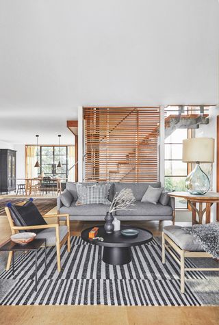 Living room with sofa and armchairs, black coffee table and black and white striped rug on wood floor
