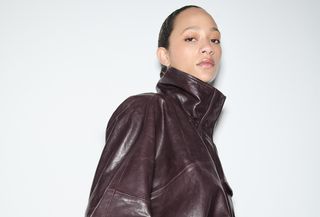 A Zara model wearing a burgundy funnel-neck cinch-waist faux leather jacket.