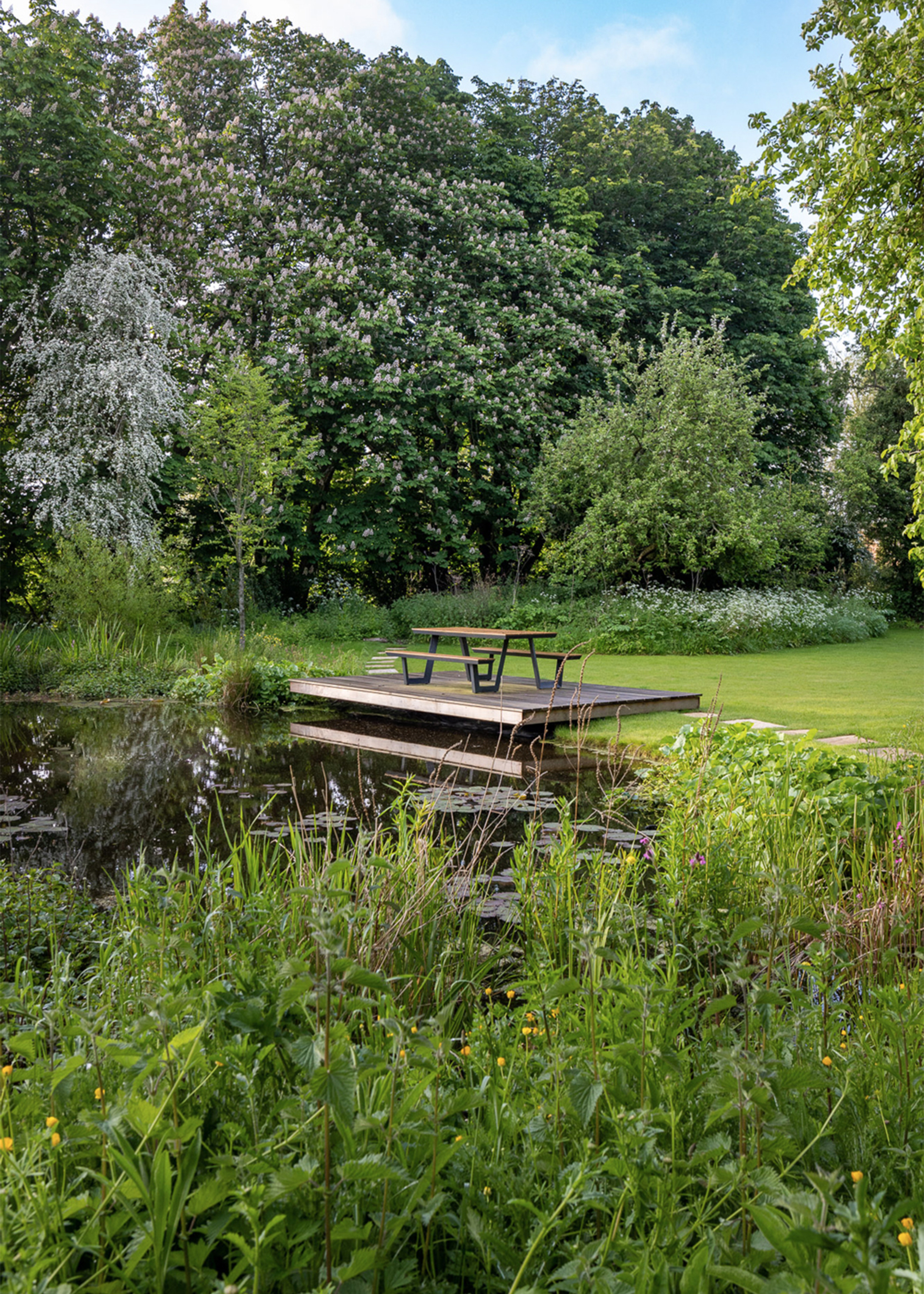 a beautiful lake side garden with a picnic bench on a wooden beam over the lake