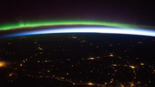 a photograph of a green and blue aurora against a sunrise with sparkling cities in Europe taken from the International Space Station