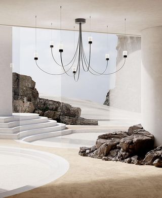 A render showing Paul Cocksedge's Gravity Chandelier for Moooi, a design featuring black curved arms hanging from the ceiling. The chandelier is installed in an imaginary room with glass walls separating the space from a desert and rocks