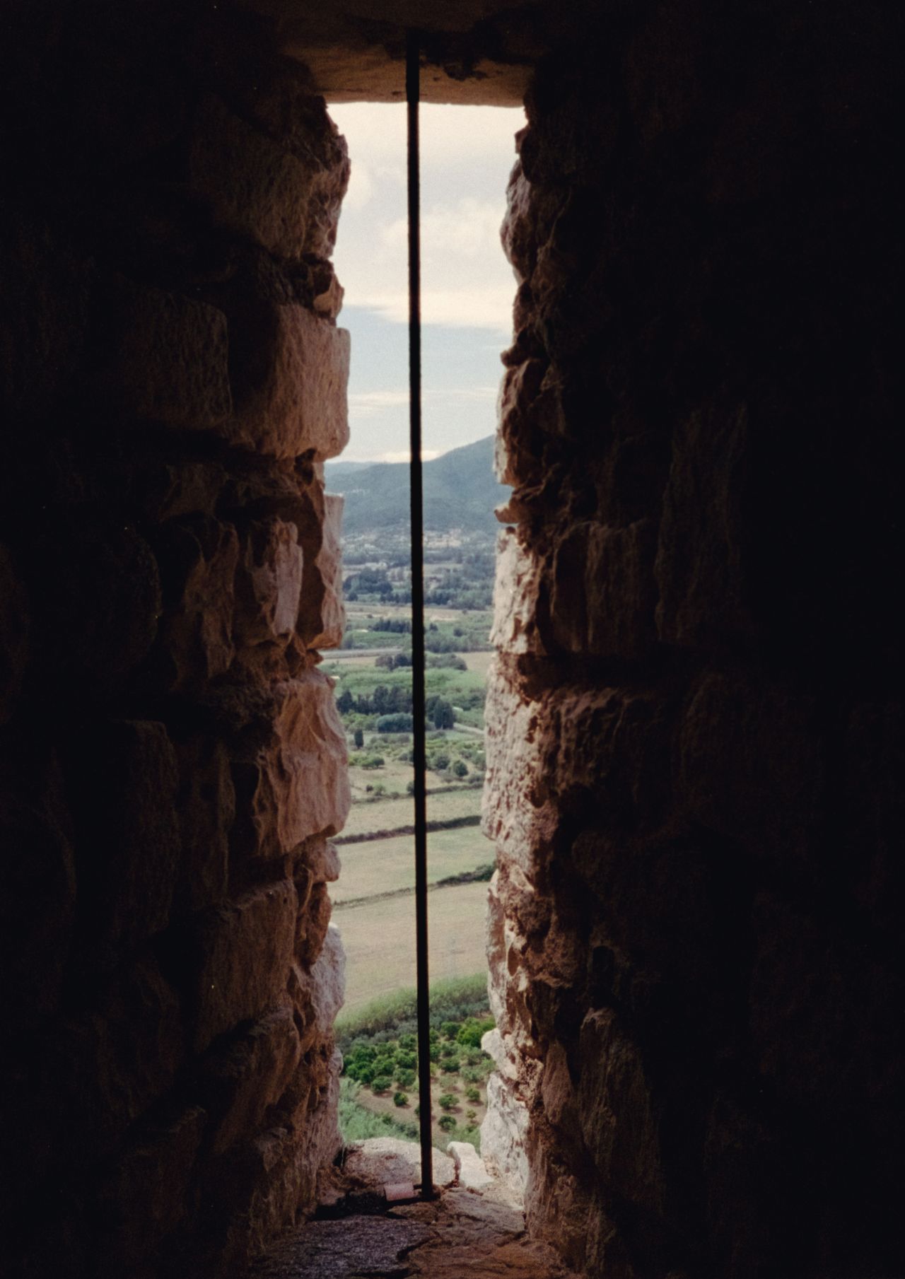 View over some fields through a narrow slit in a stone tower