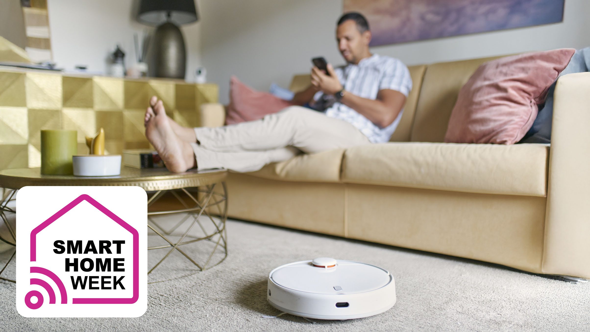 Man sitting on sofa using smartphone while robot vacuum cleans the floor