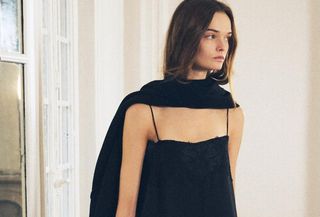 A Zara model walking in a black cape worn like a scarf, a black spaghetti strap maxi dress, and black gloves.