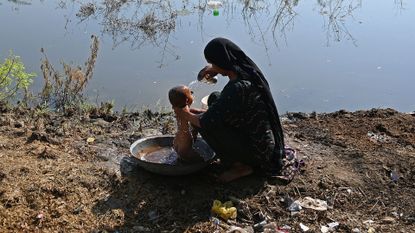 An internally displaced flood-affected woman bathes her child at a makeshift camp in Mehar city after heavy monsoon rains in Dadu district, Sindh province on September 9, 2022. - Record monsoon rains have caused devastating floods across Pakistan since June, killing more than 1,200 people and leaving almost a third of the country under water, affecting the lives of 33 million