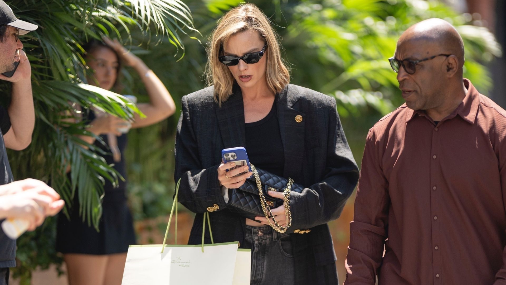 Margot Robbie walks through New York's Chinatown wearing black jeans with two-tone heels and a black oversized blazer.