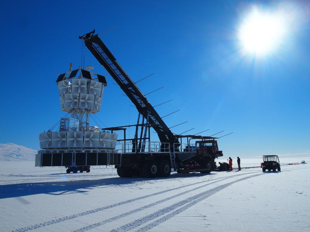 An icy landscape with a complicated piece of equipment being hoisted by a crane