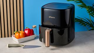 a large black 5.3 quart capacity air fryer with black touchscreen and rose gold embellishments sits upon a brown table with a blue background