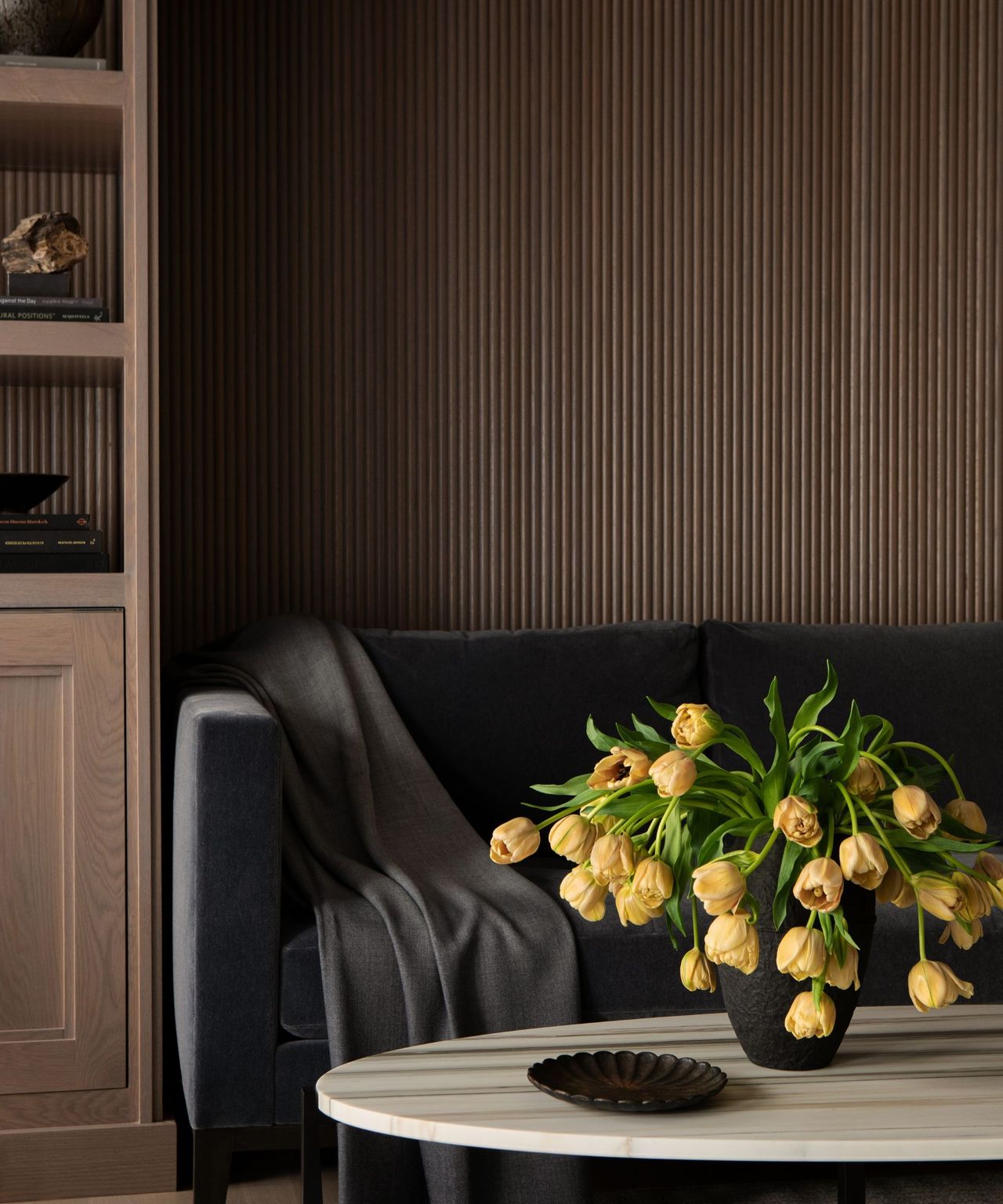A moody home office with built-in wooden shelving and a small dark gray sofa