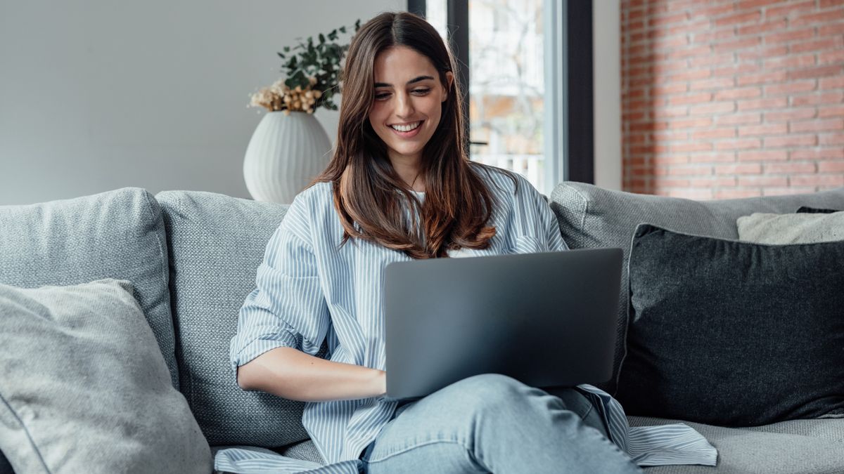 A woman sitting on a sofa and using a laptop, and she is smiling