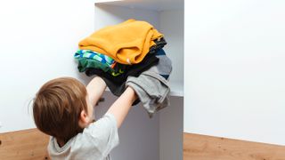 Young boy putting clothes in closet