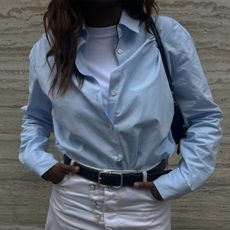 Woman wearing baby blue button-down shirt with white t-shirt underneath and white denim maxi skirt.