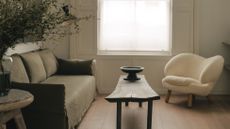 Narrow living room ideas - a white room with an olive green linen sofa facing a single white boucle armchair and crafted wooden coffee table