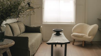 Narrow living room ideas - a white room with an olive green linen sofa facing a single white boucle armchair and crafted wooden coffee table