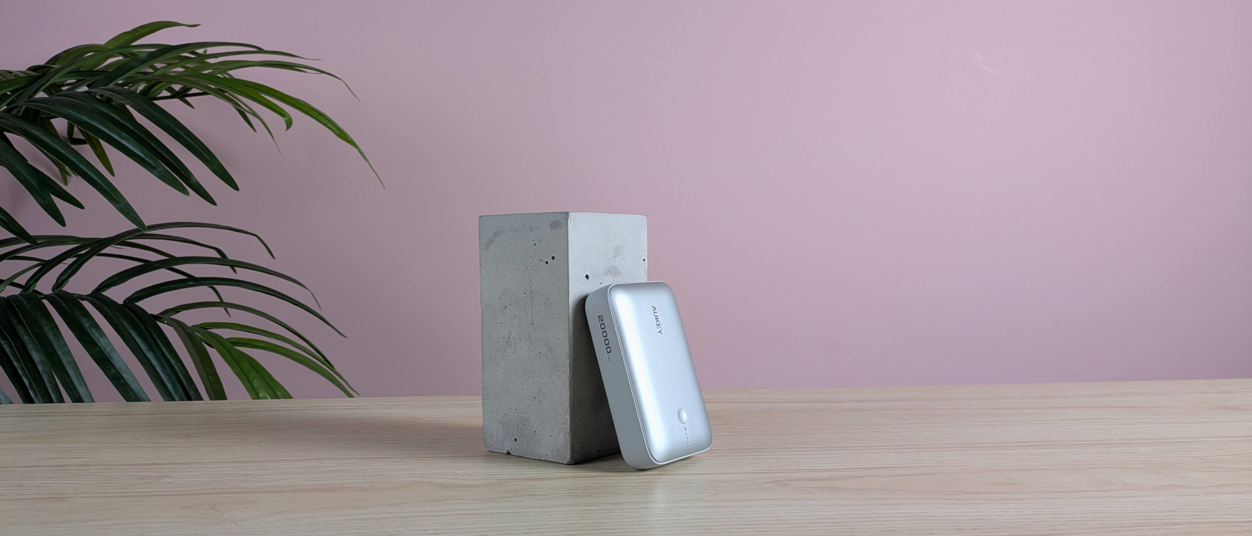 Aukey Spark Mini 20000 leaning on plinth on desk with pink wall and plant in background