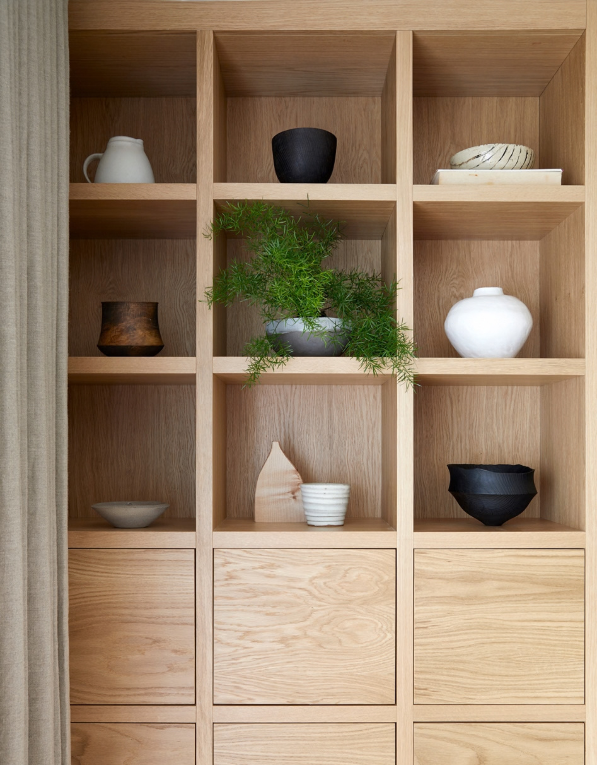 A wooden display cabinet with crafts, ceramics, and a plant