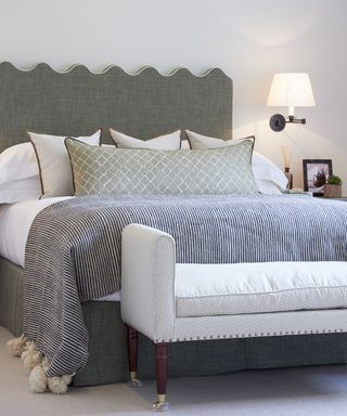 A wavy shaped gray bed headboard in a white scheme with blue and white ticking stripe throw.