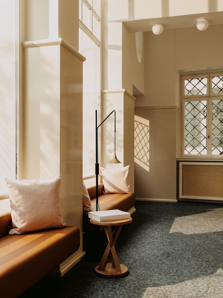 A white coffee table book sits on a wooden coffee table book in a minimalistically designed and sunlit hotel lobby.