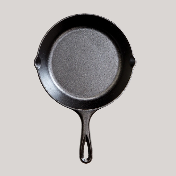 A round skillet pan in black iron sits against a pale grey background.