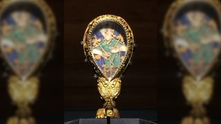 Alfred Jewel found at the Ashmolean, Oxford, U.K. Inside a teardrop shaped golden piece there is a portrait of a blonde-haired man wearing green and holding a golden rod in each hand.