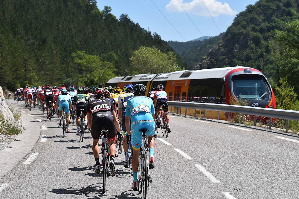 The peloton passes a train going in the opposite direction.