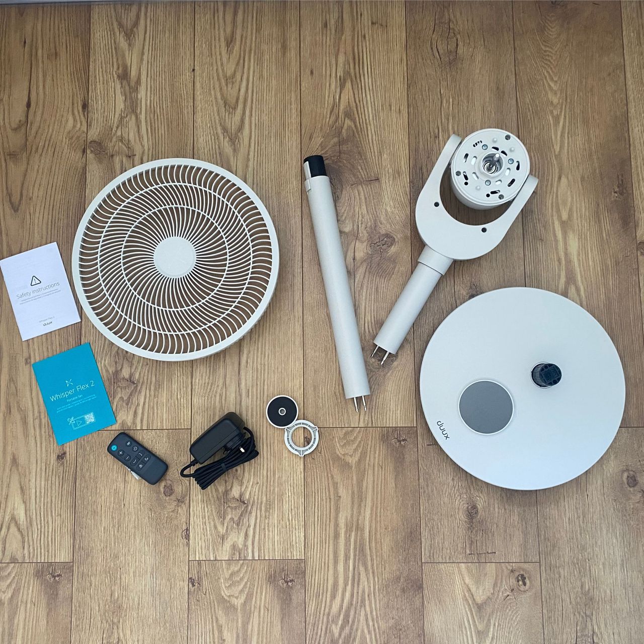 All the individual pieces of the Duux Whisper Flex 2 fan laid out on a wood-look floor